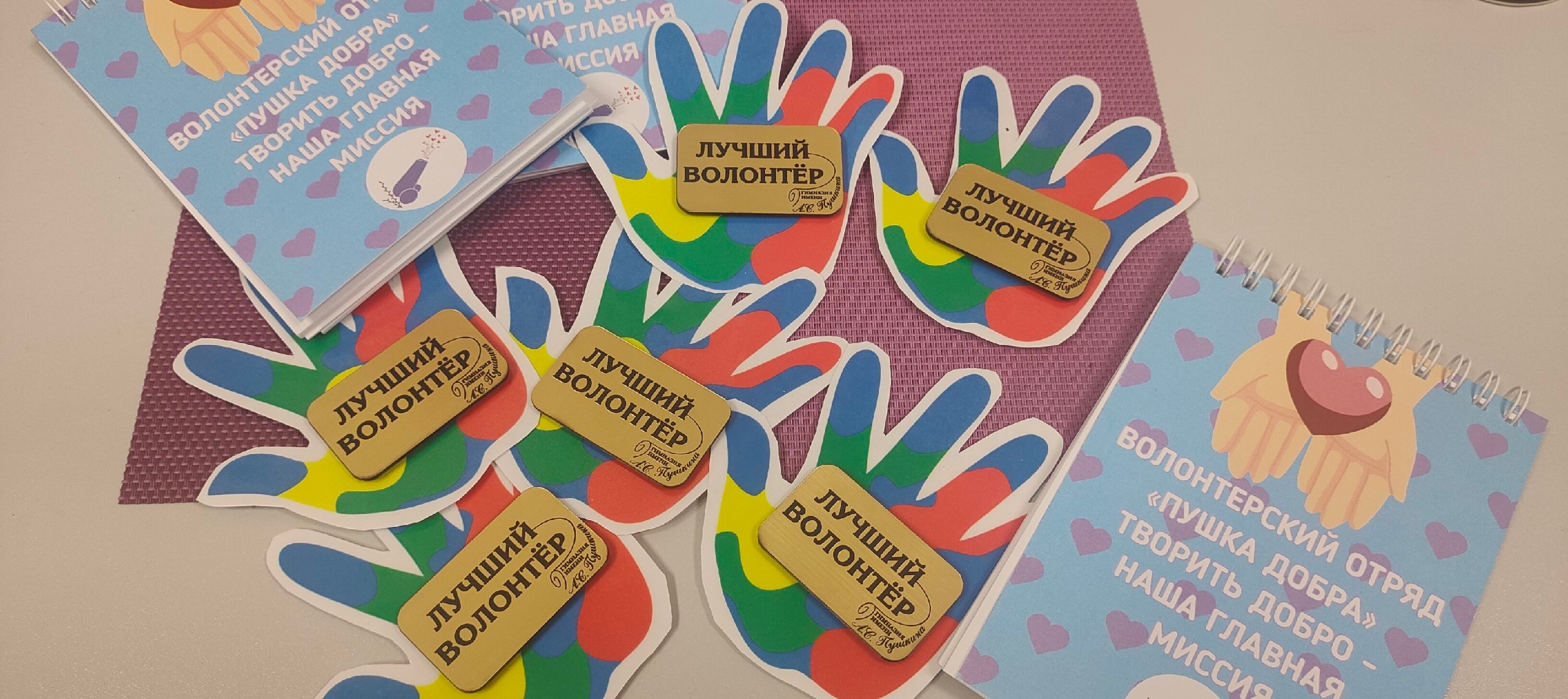 На фотографии агитационные листочки и картинки рук, на которых лежат деревянные таблички с надписью лучший волонтёр.